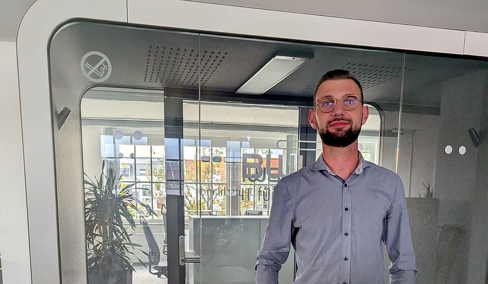 Mann (Lucas) mit Brille vor Glaswand im BWI Büro