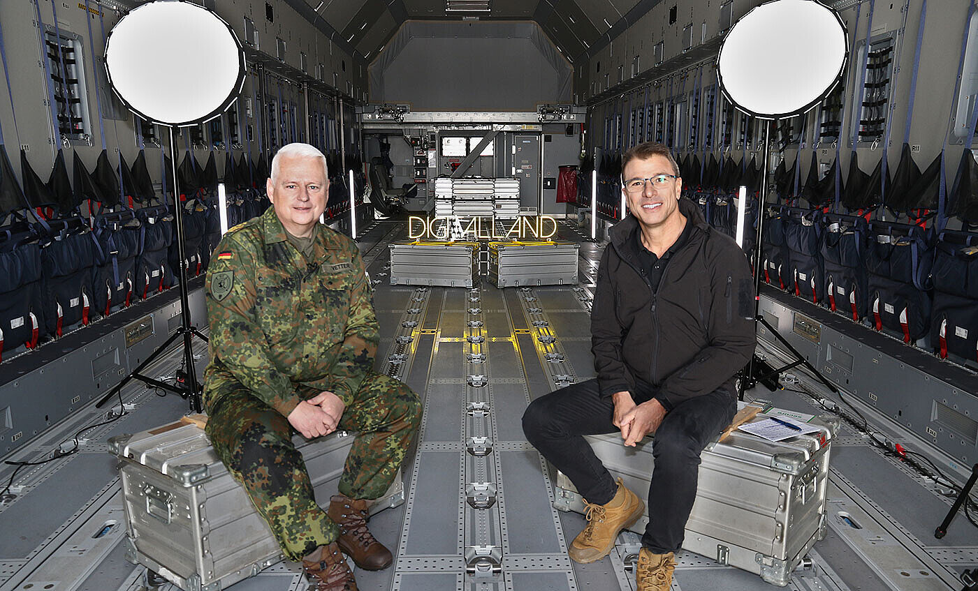 Martin Kaloudis und Generalleutnant Michael Vetter sitzen auf Kisten in der Transportmaschine A400M bereit zum drehen des Vodcastes