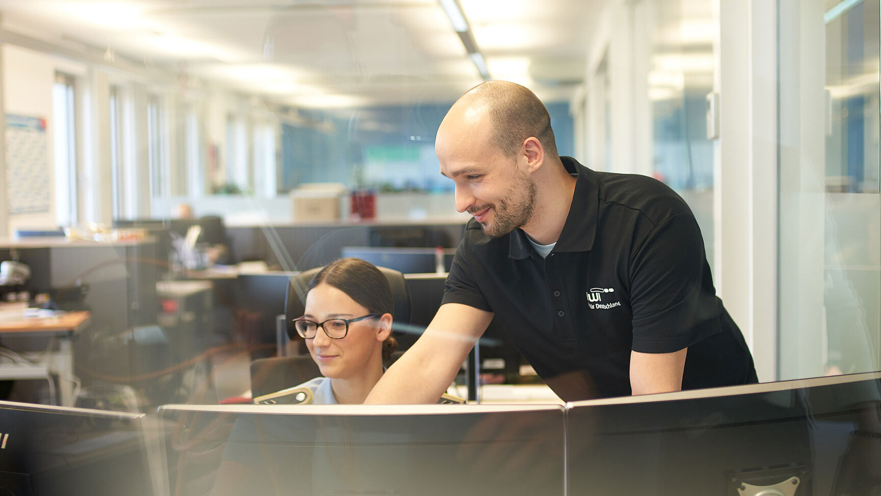 BWI-Mitarbeiter neben einer Soldatin an ihrem IT-Arbeitsplatz.