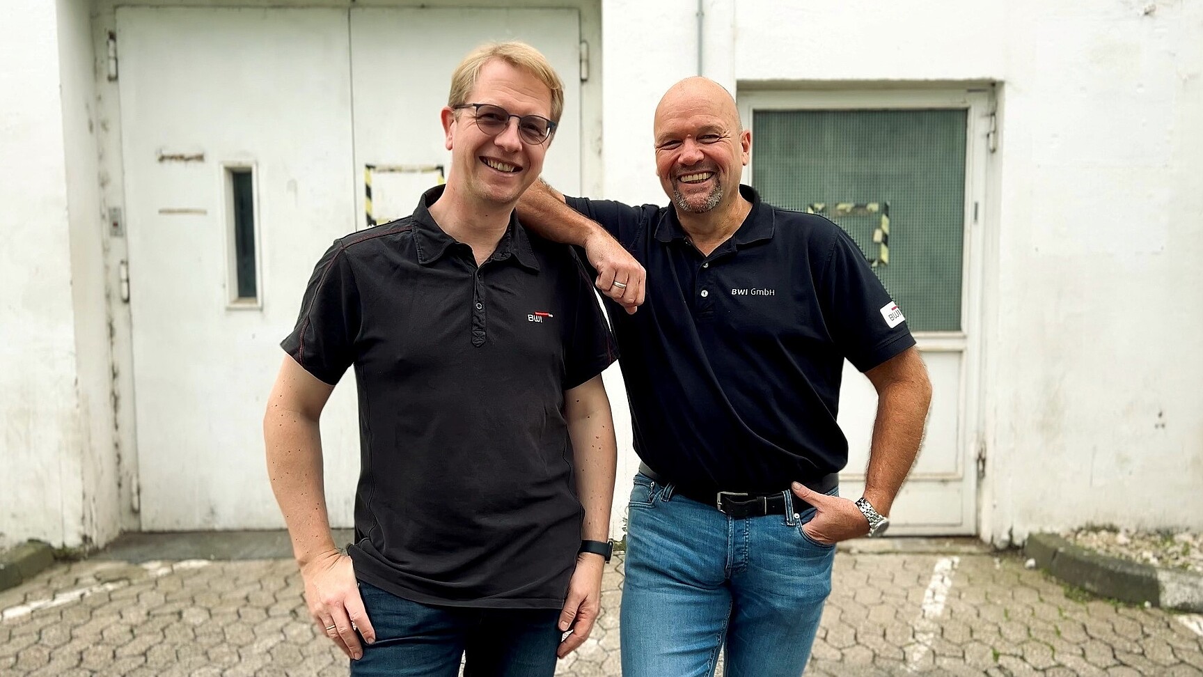 Die beiden Autoren des Beitrags vor einer weißen industriellen Außenfassade