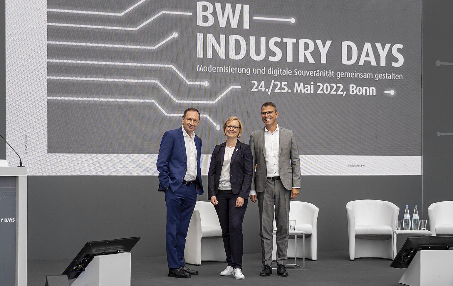 Auf einer Bühne stehen die drei Geschäftsführenden der BWI, hinter ihnen das Logo der BWI Industry Days.
