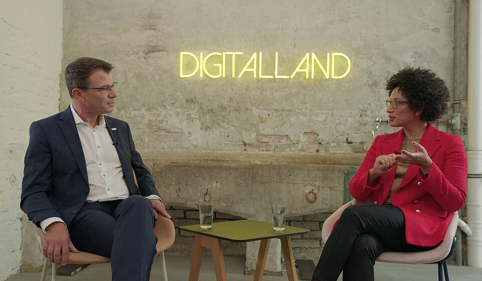 Martin Kaloudis (links) und Kenza Ait Si Abbou (rechts) sitzen zusammen vor dem Logo von Digitalland