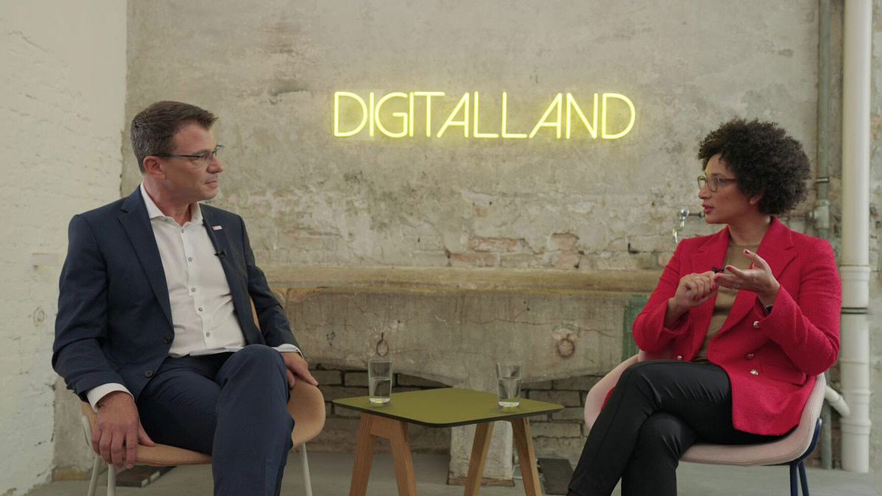 Martin Kaloudis (links) und Kenza Ait Si Abbou (rechts) sitzen zusammen vor dem Logo von Digitalland