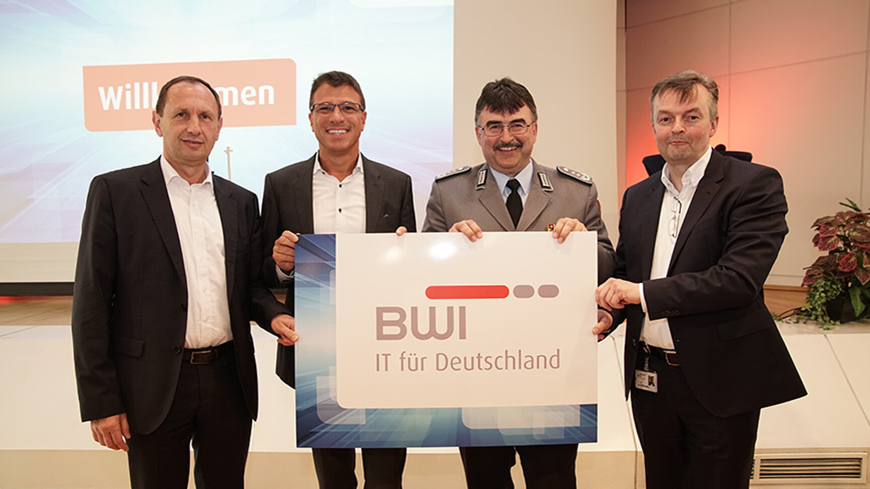 Vier Männer halten ein Plakat mit dem BWI-Logo. Frank Leidenberger (CSO BWI), Martin Kaloudis (CEO BWI), Oberst Hans-Jürgen Neubauer (BAIUDBw) und Bernd Klinder (COO BWI)