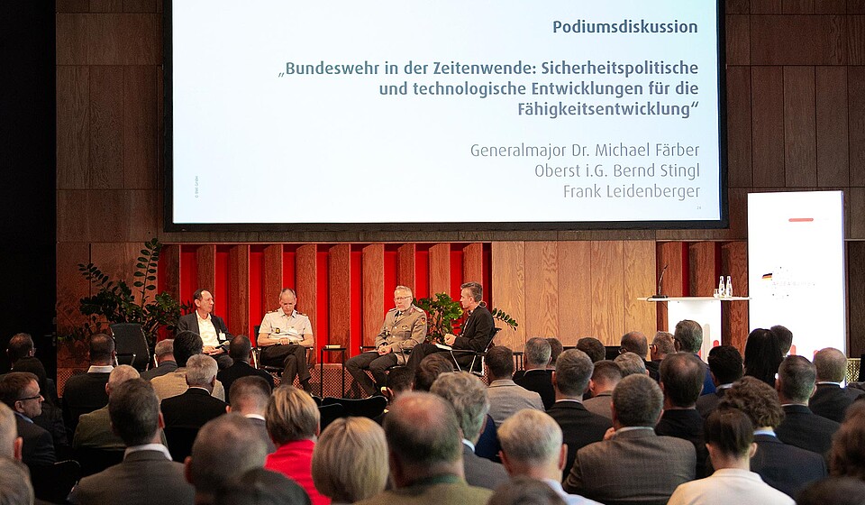 Bild von Teilnehmenden einer Podiumsdiskussion auf einer Bühne vor Zuschauenden