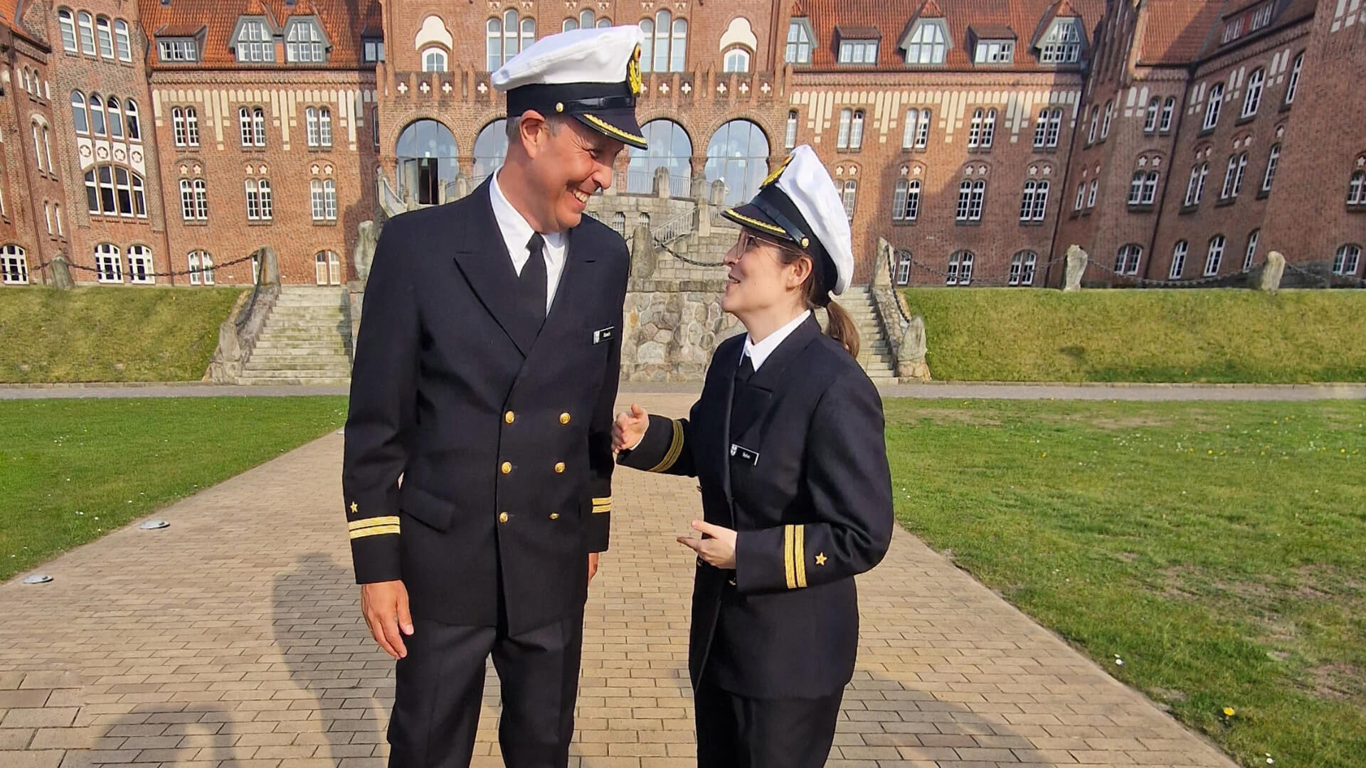 Ein Mann und eine Frau in Uniform vor dem Gebäude der Marineschule Mürwik.